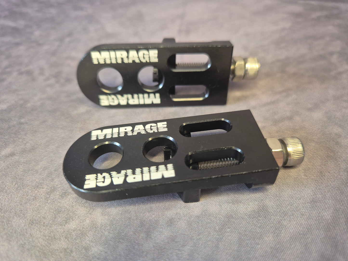 Two black metal chain tensioner components with 'Mirage' branding on a grey background